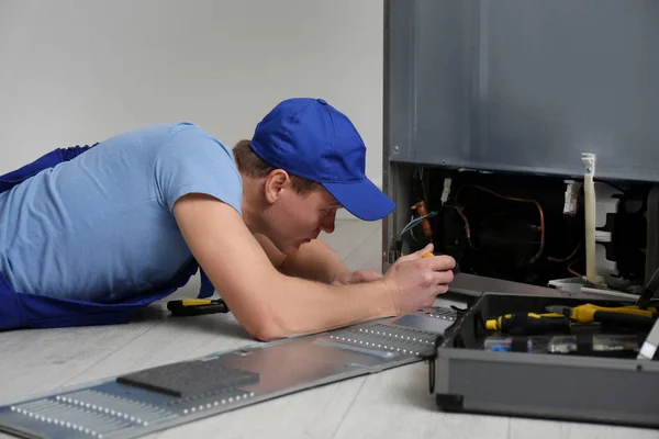 Manlig tekniker med skruvmejsel reparera kylskåp inomhus — Stockfoto