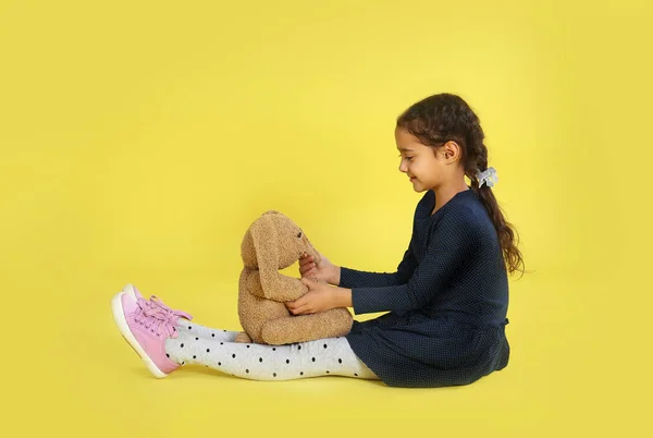 Menina bonito com coelho de brinquedo no fundo amarelo — Fotografia de Stock