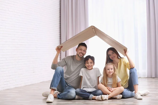 Happy family sitting under cardboard roof at home. Insurance con — Stock Photo, Image