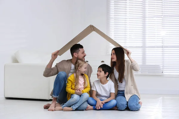 Šťastná rodina sedí doma pod lepenkovou střechou. Ikona pojištění — Stock fotografie