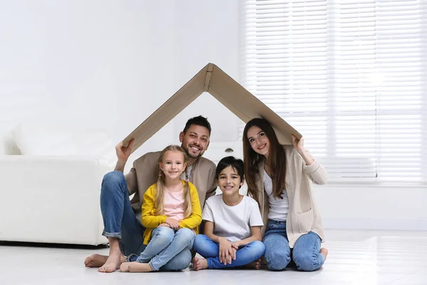 Happy family sitting under cardboard roof at home. Insurance con