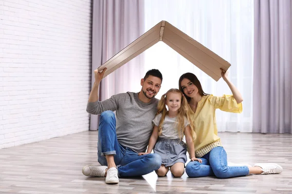 Feliz familia sentada bajo el techo de cartón en casa. Seguro con —  Fotos de Stock