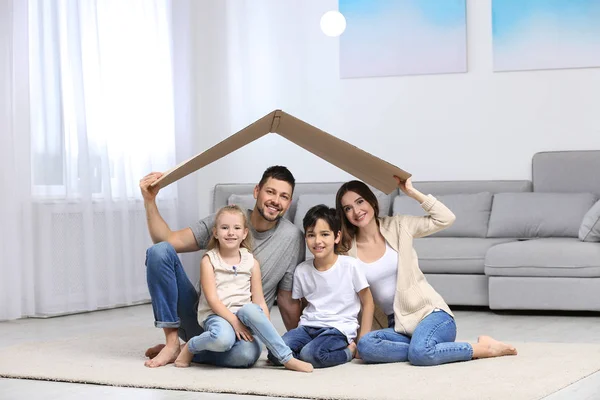 Szczęśliwa rodzina siedzi pod kartonowym dachem w domu. Przekręt ubezpieczeniowy — Zdjęcie stockowe