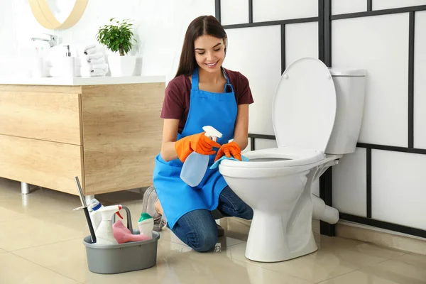 Wanita muda membersihkan toilet mangkuk di kamar mandi — Stok Foto