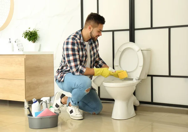 Молодой человек чистить унитаз в ванной комнате — стоковое фото
