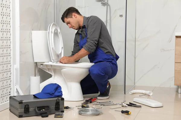 Professional plumber working with toilet bowl in bathroom — 스톡 사진