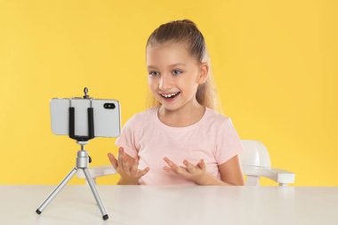 Sarı arka plandaki masada video kaydeden sevimli küçük blogcu.