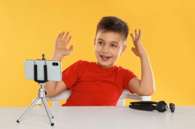 Cute little blogger recording video at table on yellow background clipart