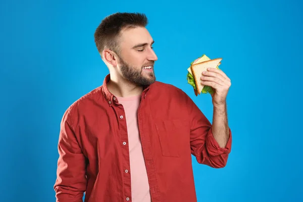 Young man with tasty sandwich on light blue background — Stock Photo, Image