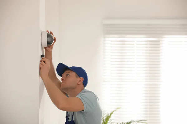 Техник устанавливает камеру видеонаблюдения на стене в помещении — стоковое фото