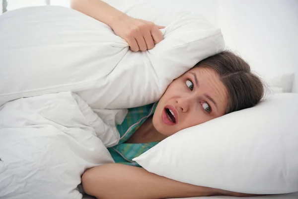 Emocional mujer joven cubriendo las orejas con almohadas en casa en la mañana — Foto de Stock