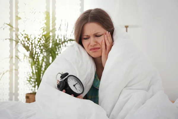 Mujer joven soñolienta con despertador en casa por la mañana — Foto de Stock