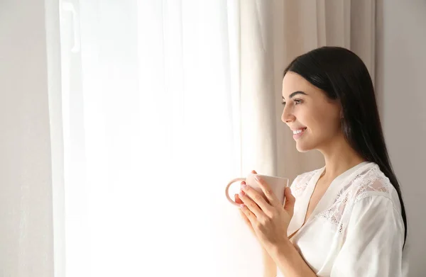 Jeune femme avec une tasse de café près de la fenêtre. Lazy matin — Photo