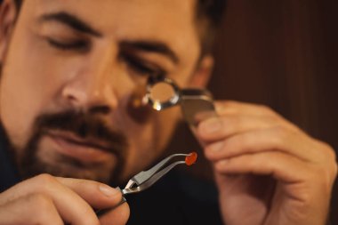 Bulanık arkaplanda mücevher ile çalışan kuyumcu, yakın plan