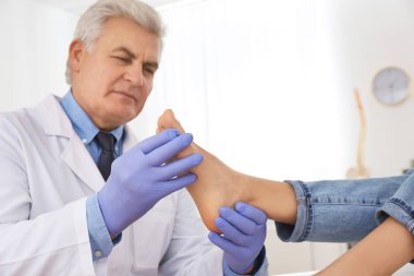 Erkek ortopedist klinikte hastanın ayağını kontrol ediyor.