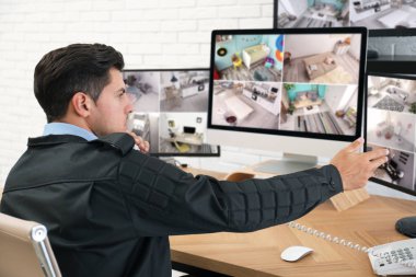 Erkek güvenlik görevlisi iş yerindeki monitörlerin yanında telefonla konuşuyor.