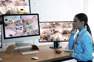 İş yerindeki monitörlerin yanında telefonla konuşan kadın güvenlik görevlisi.