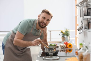 Genç adam mutfakta lezzetli bir çorba pişiriyor.