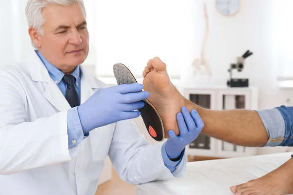 Мужчина ортопед, устанавливающий стельку на ногу пациента в клинике — стоковое фото