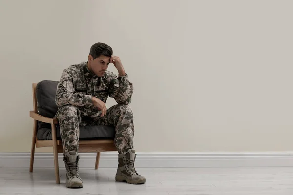 Gestresste militaire officier zit in fauteuil in de buurt van witte muur in — Stockfoto