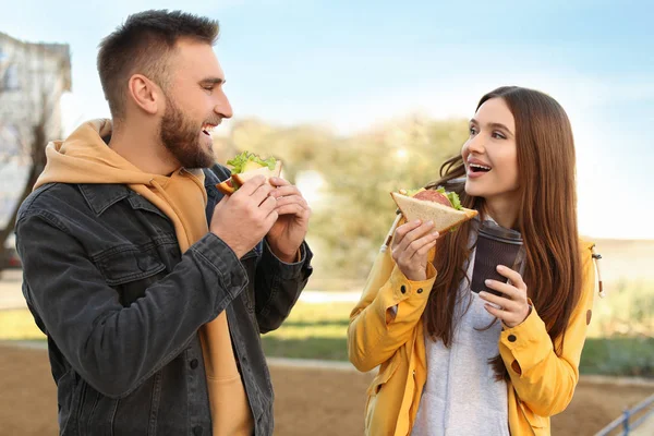 Счастливая молодая пара с бутербродами и кофе на городской улице — стоковое фото