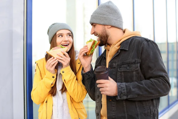 Счастливая молодая пара с бутербродами и кофе на городской улице — стоковое фото
