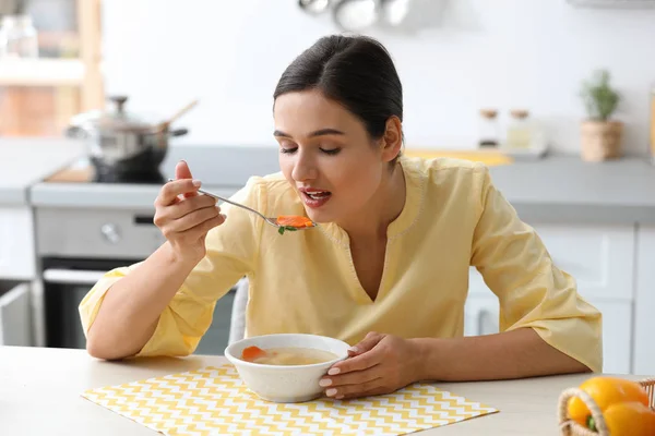 Молодая женщина ест вкусный овощной суп за столом на кухне — стоковое фото