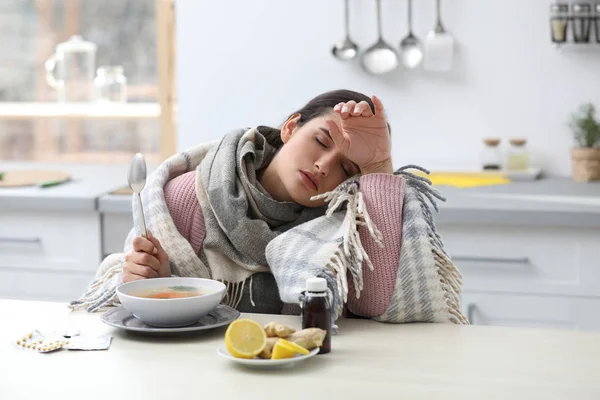 Больная молодая женщина ест суп, чтобы вылечить грипп за столом на кухне — стоковое фото