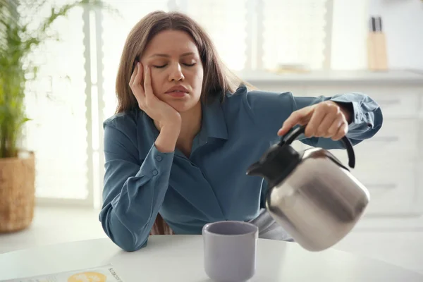 Сонная молодая женщина наливает кофе в чашку дома утром — стоковое фото