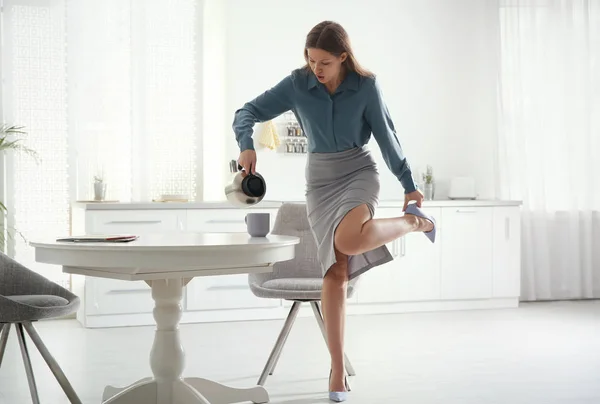 Jonge vrouw gieten koffie in beker terwijl het zetten van op schoenen bij ho — Stockfoto