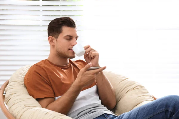 Attraktiver Mann entspannt sich im Papasan-Stuhl am Fenster zu Hause — Stockfoto