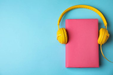 Açık mavi arka planda kitap ve kulaklıklar, düz yatış. Metin için boşluk