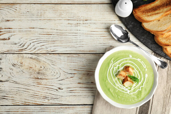 Delicious broccoli cream soup with croutons served on white wooden table, flat lay. Space for text