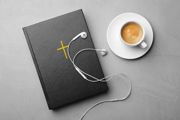 Bible, cup of coffee and earphones on light grey background, flat lay. Religious audiobook