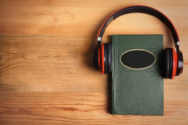 Libro y auriculares modernos en mesa de madera, vista superior. Espacio para —  Fotos de Stock