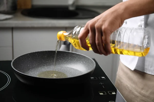 Man pouring cooking oil from bottle into frying pan, closeup