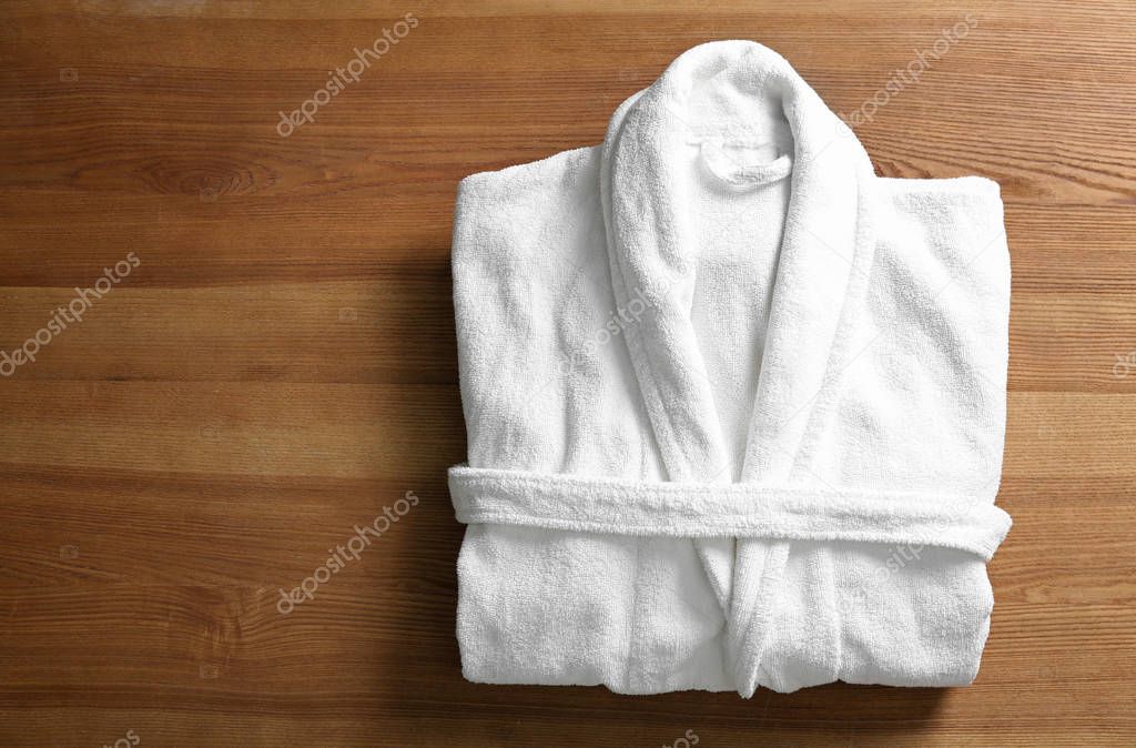 Clean folded bathrobe on wooden background, top view
