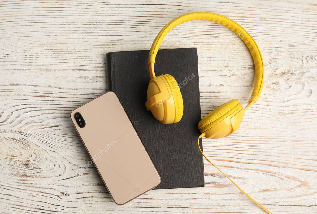 Book, modern headphones and smartphone on white wooden table, fl