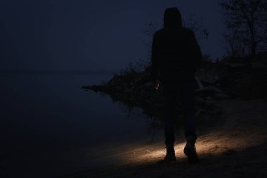 Akşamları elinde fener olan bir adam nehir kenarında yürüyor.
