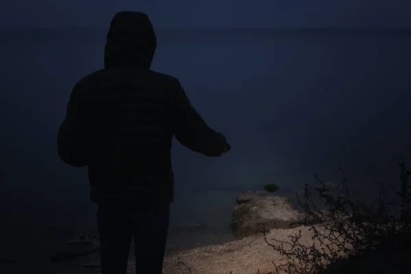 懐中電灯を持った男が夜に川の近くを歩く — ストック写真