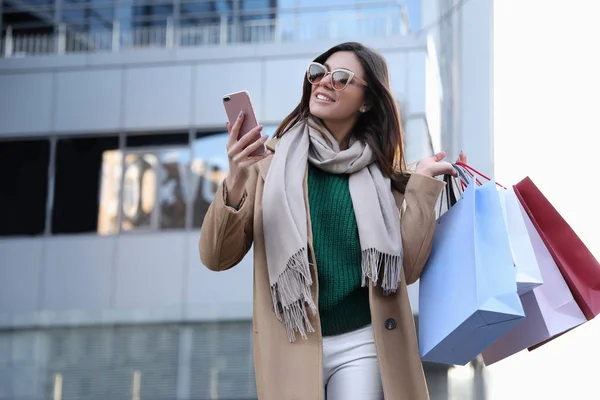 Alışveriş çantaları ve akıllı telefonları olan güzel bir kadın. — Stok fotoğraf