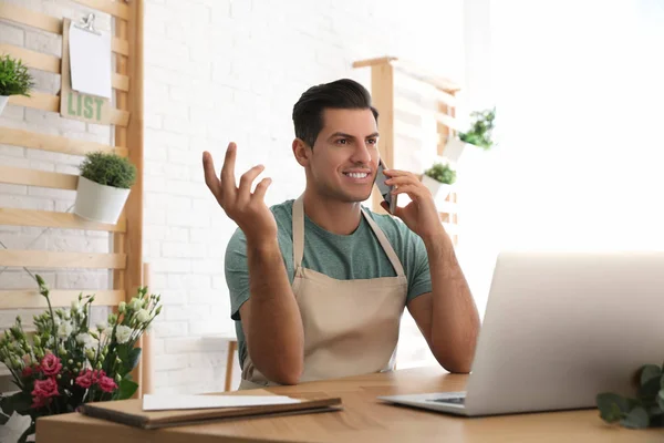 Florist talking on smartphone near laptop in workshop — 스톡 사진