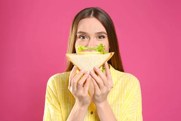 Młoda kobieta je smaczne kanapki na różowym tle — Zdjęcie stockowe