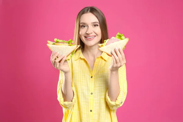 Młoda kobieta ze smacznymi kanapkami na różowym tle — Zdjęcie stockowe