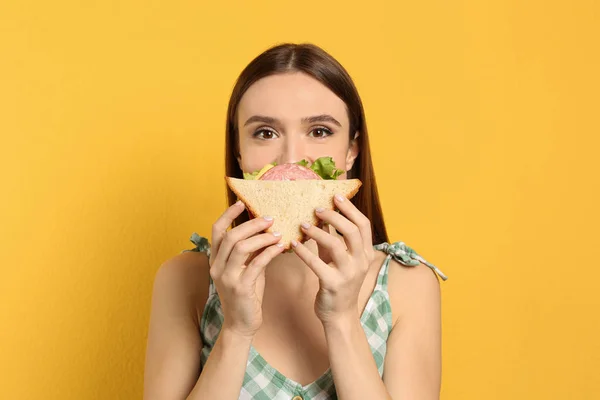 若い女性食べるおいしいサンドイッチ上の黄色の背景 — ストック写真