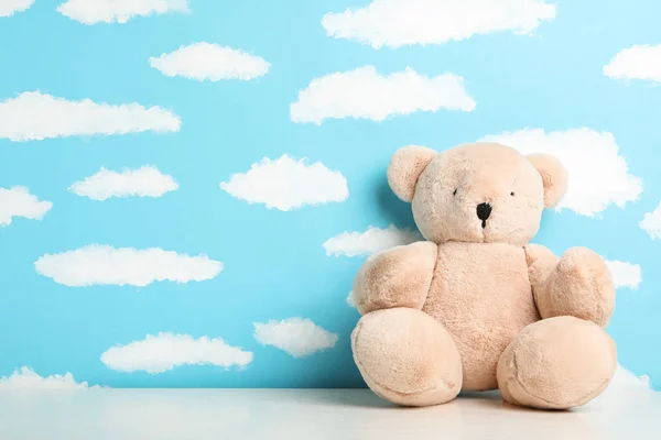 Teddy bear on white table near wall with painted blue sky, space — Stock Photo, Image