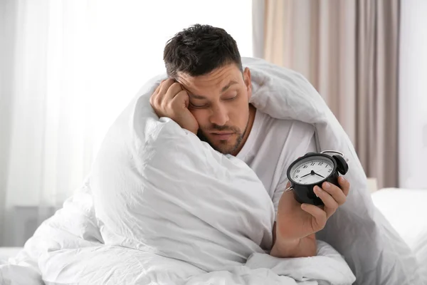 Sleepy man with alarm clock at home in morning