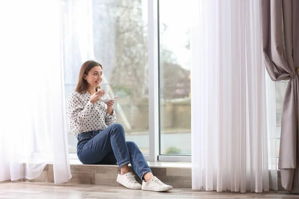 Mujer joven con taza cerca de la ventana interior —  Fotos de Stock