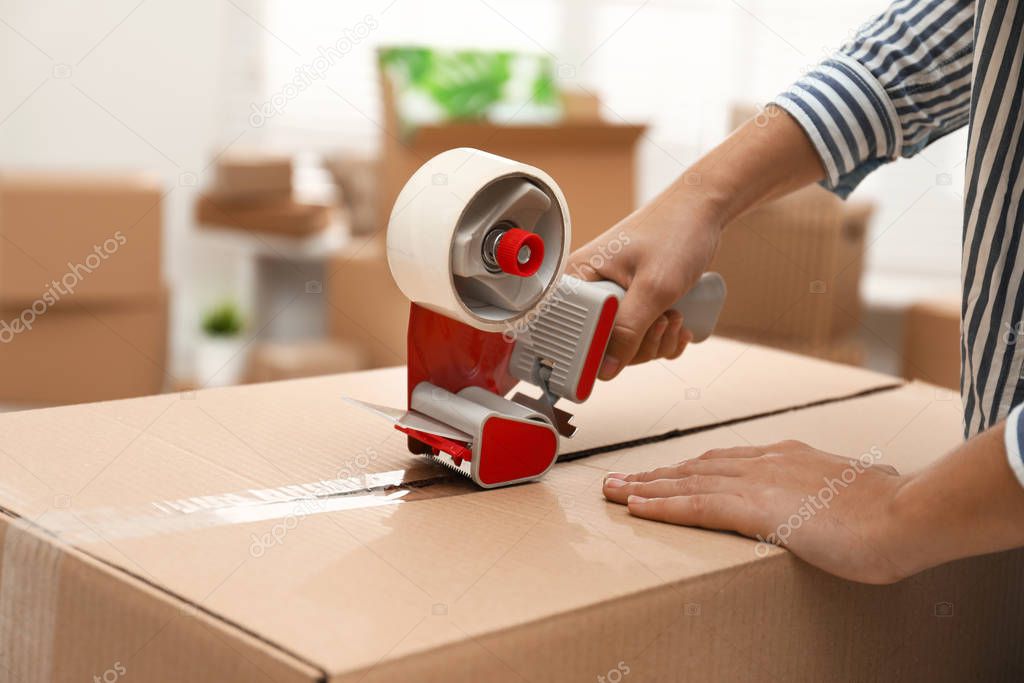 Woman packing cardboard box indoors, closeup. Moving day