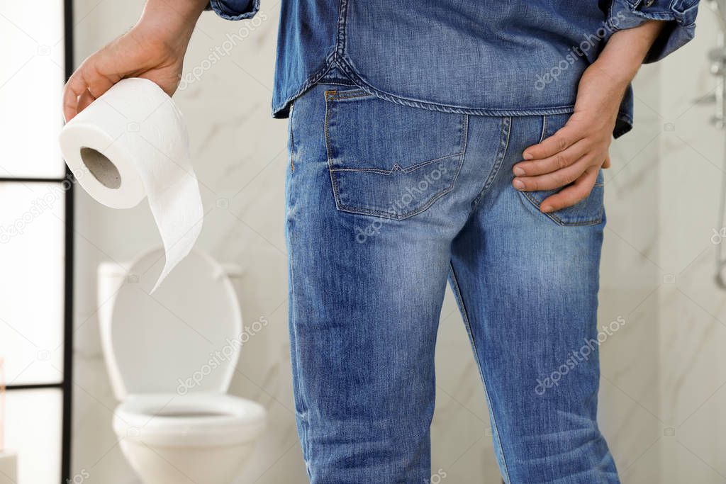 Man with toilet paper suffering from hemorrhoid in rest room, closeup